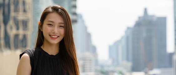 Happy young beautiful Asian businesswoman against view of the city