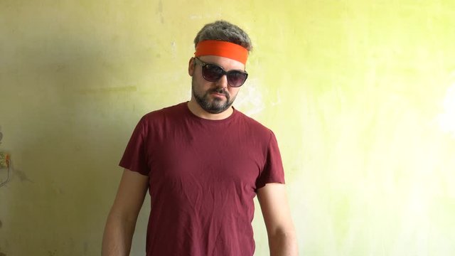 The bearded man stands against the wall in dark glasses