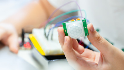 Closeup, Hands of teenage student hold PIR sensor connected to breadboard and microcontroller with...
