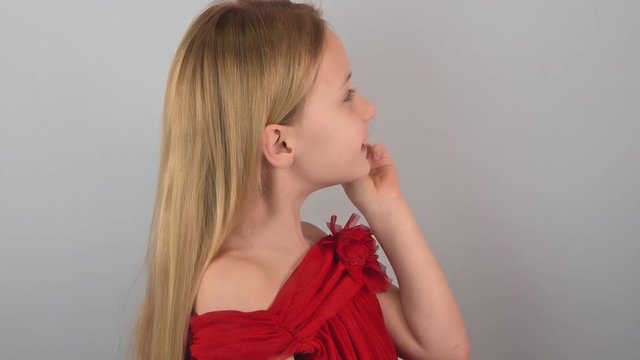 Side view funny cute little caucasian blond girl doing trick - swallowing candy on a stick on the gray background. Concept children's tricks and jokes