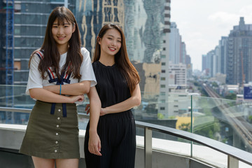Fototapeta na wymiar Two young beautiful Asian teenage girls together against view of the city