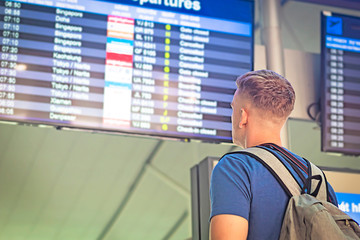 Tourist guy or man with a backpack looks at the scoreboard at the airport or train station