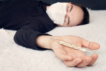 Man with acute male cold measures fever. sick person in wearing a protective medical mask in bed is...