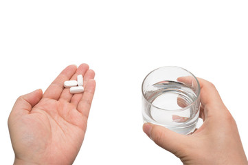 A man's hand holding a white pill and a cup of water in hand on a white background.