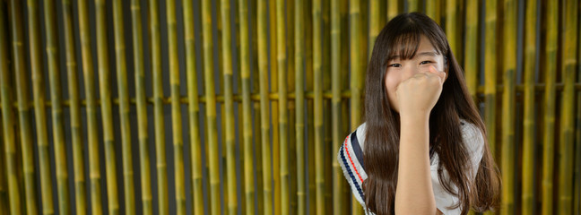 Fototapeta na wymiar Young beautiful Asian teenage girl against bamboo fence