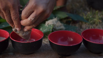 local young black man preparing kava juice drink at a tropical island of Vanuatu in the south pacific ocean during the afternoon by squeezing it to small cups