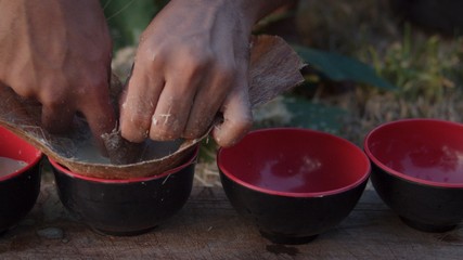 local young black man preparing kava juice drink at a tropical island of Vanuatu in the south pacific ocean during the afternoon by squeezing it to small cups