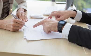 Businessman and businesswoman holding pen and pointing analysis report on wooden table in office