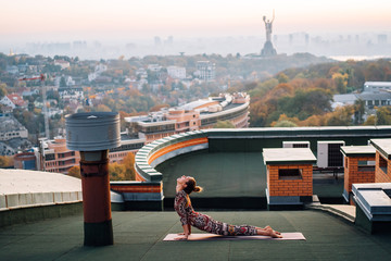 Woman doing yoga on the roof of a skyscraper in big city.
