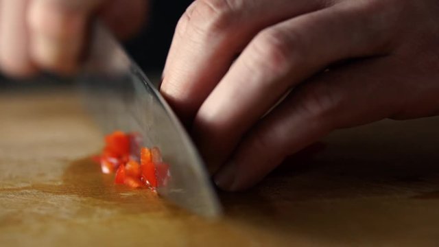 Male hands dicing red bell pepper with sharp knife brunoise style on wooden chopping board, SLOW MOTION