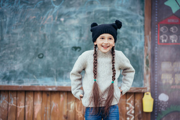 Little girl in a hat posing on the background of the school blackboard