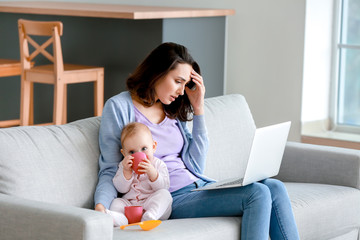 Young woman with laptop suffering from postnatal depression at home