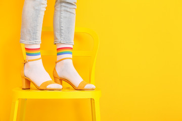 Legs of young woman in socks and sandals standing on chair against color background