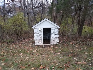 small white stone shed with leaves and forest