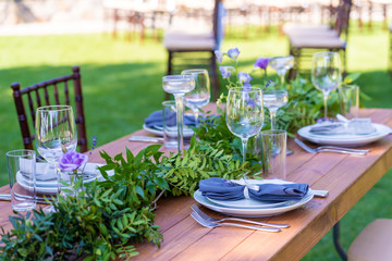 Beautifully decorated wooden table in a summer open-air cafe. Green branch and fresh flowers table decoration