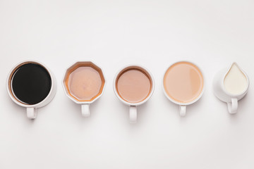 Cups of different coffee and jug with milk on light background