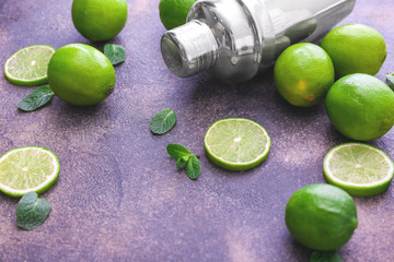 Fresh limes, shaker and ice cubes on grey background