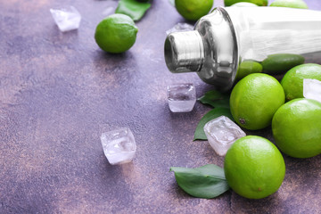 Fresh limes, shaker and ice cubes on grey background