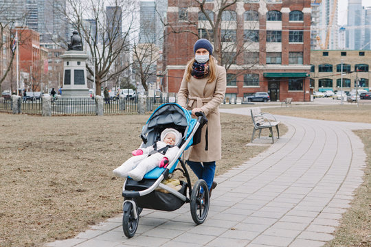 Young Caucasian Mother In A Surgical Mask Walking With Baby Outdoor In Toronto. Protective Face Mask Precaution Against New Chinese Atypical Pneumonia COVID-19 Epidemic Virus Disease.