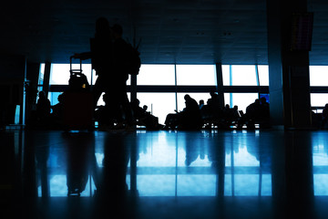 Silhouettes of people walk in front of a large stained glass window. People at the airport walk along the corridor
