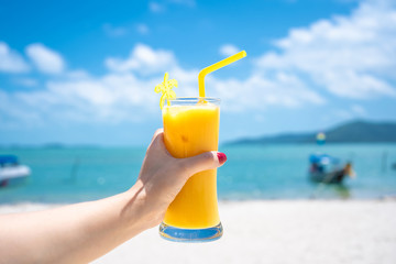 First-person view. Girl holds a glass cup of cold mango fresh on the background of a sandy tropical beach. White sand and a boat. Fairytale vacation in Thailand