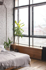 Eclectic bedroom interior with tropical plants. White brick wall and wooden floor.