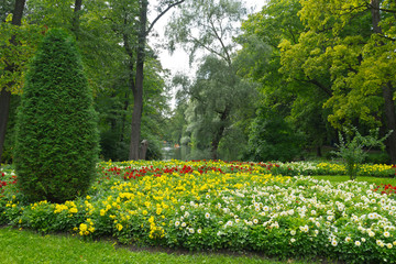 St. Petersburg in summer. Beautiful city park with flower beds and green trees near the pond on Elagin Island. In the distance, people relax in boats on a pond. Park landscape