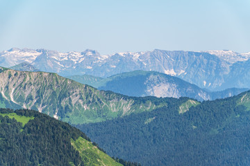 Green mountain ridges, surrounded by high mountains. Snow-capped mountain peaks on the horizon. Layers of mountains in the haze. Krasnaya Polyana, Sochi, Caucasus, Russia.