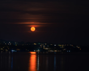 Red full moon in the night sky over sea and houses on the beach 