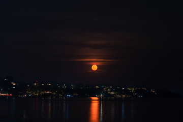 Fototapeta na wymiar Red full moon in the night sky over sea and houses on the beach 
