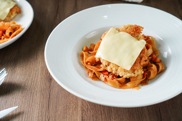 Pasta, Italian food, with tomato sauce topping with deep fried crispy pork cutlet and a sheet of cheese in white dish place on dark brown wooden table........