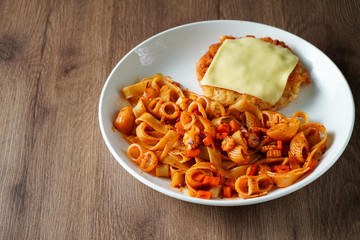 Pasta, Italian food, with tomato sauce topping with deep fried crispy pork cutlet and a sheet of cheese in white dish place on dark brown wooden table