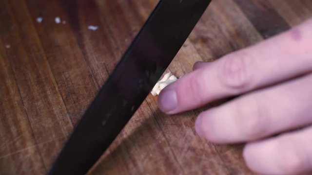 Crushing a piece of garlic with a knife and cutting it