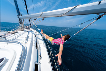 Fototapeta na wymiar Young man enjoys tropical sailing in the hammock set on the boom of the yacht