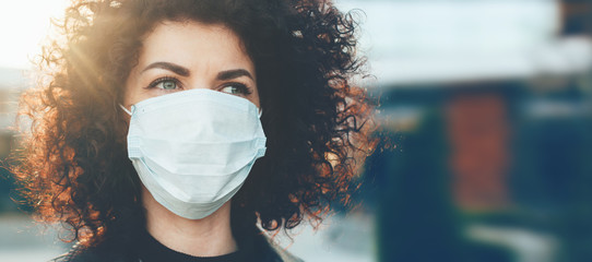 Lovely curly haired caucasian lady protecting herself from viruses while wearing special mask - obrazy, fototapety, plakaty