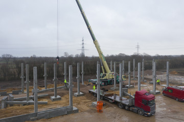 huge concrete pillars are erected on a large construction site using a crane