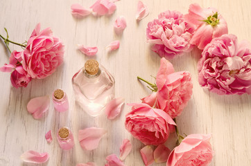 Obraz na płótnie Canvas Rose water in glass bottle and pink flowers with petals on white wooden background. SPA or aromatherapy concept