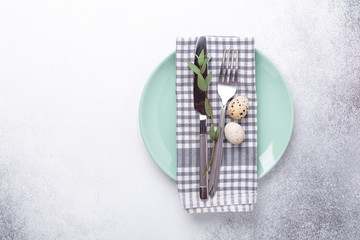 Easter table setting. Empty mint and white plates, linen napkin, eucalyptus leaves and quail eggs on stone background