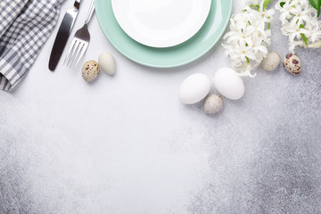 Obraz na płótnie Canvas Beautiful Easter table setting in Scandinavian style. Green mint plate, eggs and silver cutlery on modern concrete background with hyacinth. Copy space. Top view