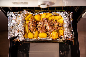 in oven potatoes and pork neck in foil. view top. 