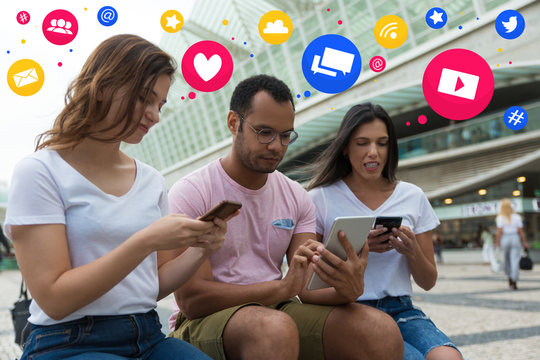 Group of young people using devices on street. Calm friends sitting with smartphones and tablet with social media network icons above. Technology concept