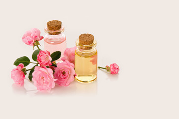 Rose flower oil and water in glass bottles fresh pink flowers on branch with leaves on white background with copy space. Aromatherapy or SPA concept