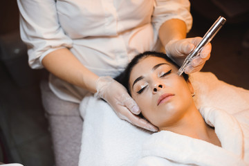 Obraz na płótnie Canvas Skin care procedure session done in a spa salon on the face of a brunette caucasian woman with closed eyes using an apparatus