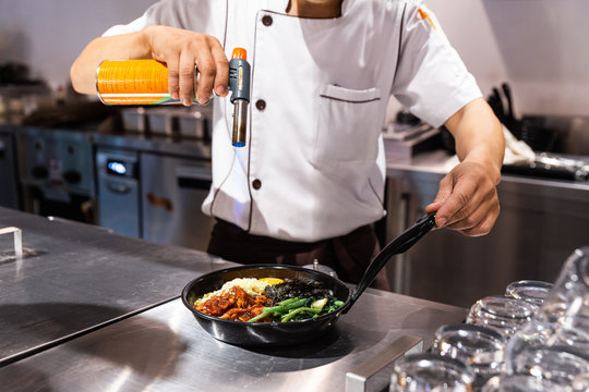 Bibimbap (Korean rice mixed with kimchi pork, seaweed and stir fried vegetables topping with sesame) served on the hot pan that chef using a blow torch for melting mozzarella cheese on a fried egg.