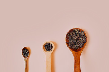 Three wooden vintage spoons of different sizes filled with dry granules and dried tea leaves on a...