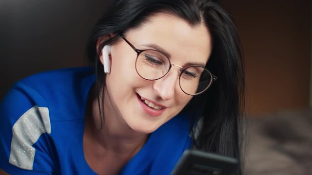 Woman in wireless earphones talking on video call use smartphone. Close up shot on 4k RED camera