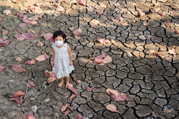 Little girl wearing medical face mask standing at dry cracked pond during dry season.