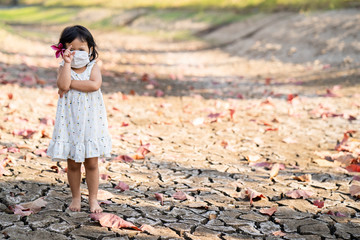 Little girl wearing medical face mask standing at dry cracked pond during dry season.