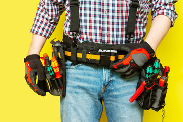 Electrician or professional Builder in the installer's belt with tools on a yellow background....