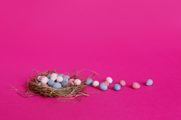 Bright colorful Easter eggs in a bird's nest on a pink background with space for text. The concept of Easter, spring, holiday. Side view